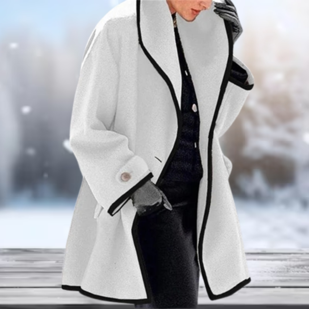 Manteau blanc élégant avec bordure noire, porté par une personne en gants noirs, sur fond de paysage enneigé. Mode hiver chic et sophistiquée.