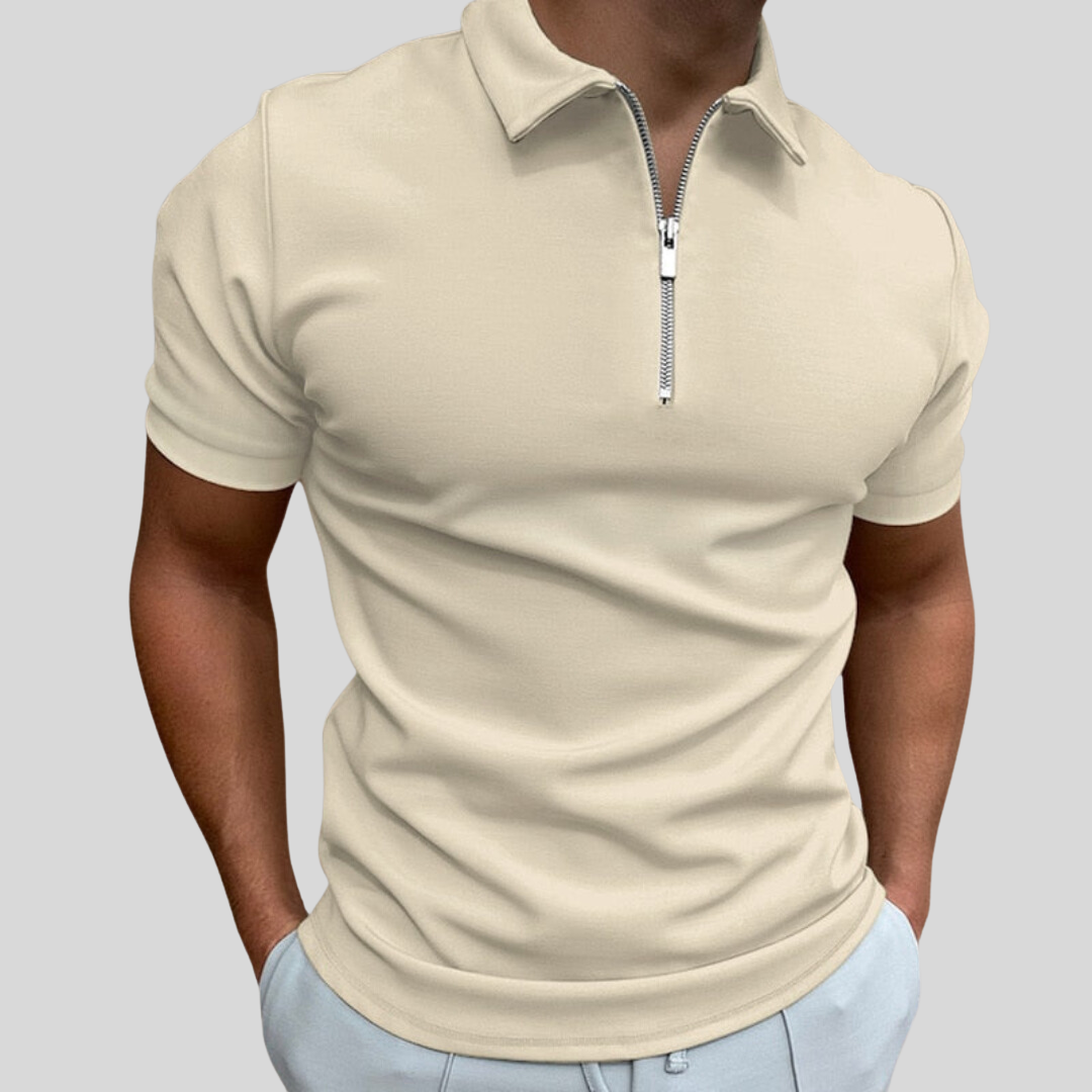 Homme portant un polo beige à fermeture éclair, manches courtes, sur fond gris. Mode masculine élégante, tenue décontractée chic.