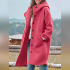 Femme portant un manteau rose en laine bouclée avec capuche, debout en extérieur. Mode automne-hiver, style décontracté, tendance vestimentaire.