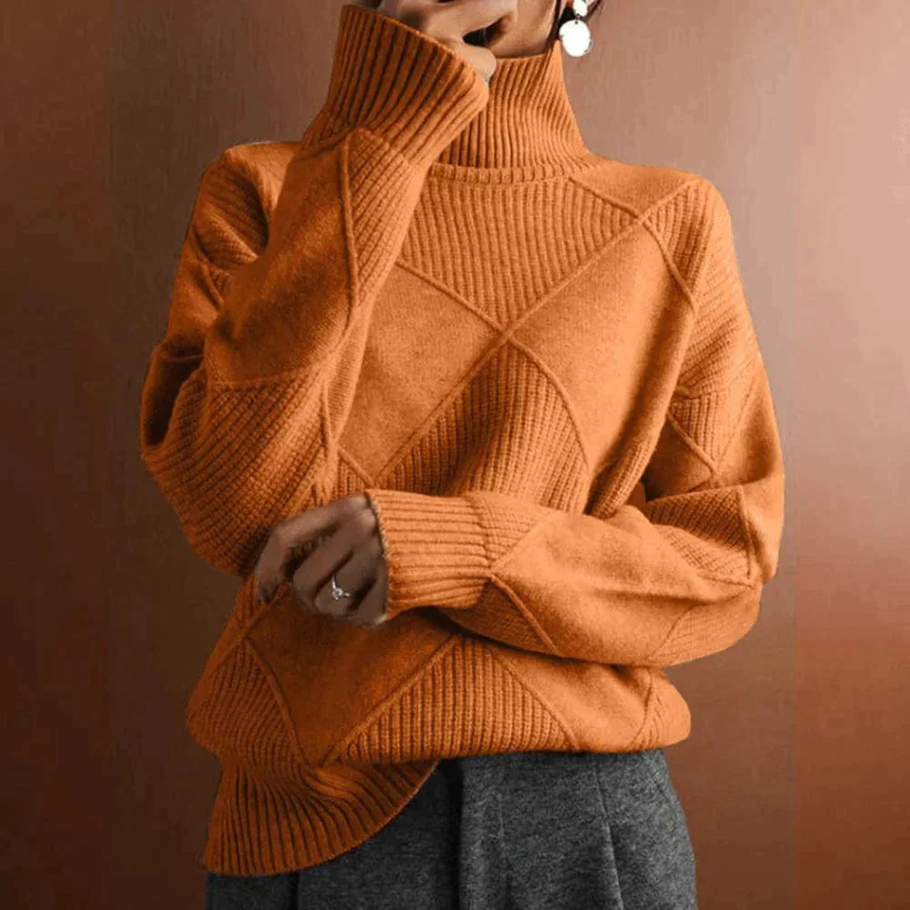 Femme portant un pull en laine orange à col roulé, motif géométrique, manches longues, devant un fond marron. Mode automne-hiver tendance.