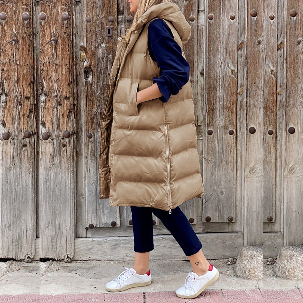 Femme portant une doudoune longue beige avec capuche, posant devant une porte en bois rustique. Mode automne-hiver, style décontracté, tendance.