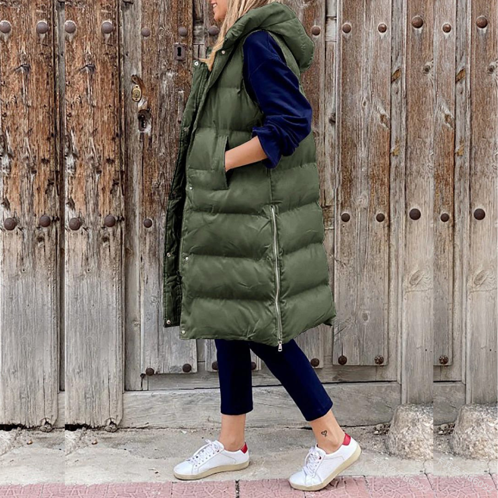 Femme portant une doudoune longue verte avec capuche, devant une porte en bois rustique. Mode automne, style décontracté, tendance vestimentaire.