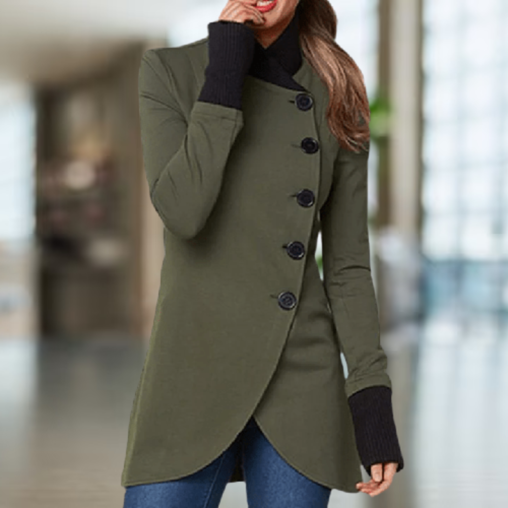 Femme portant un manteau vert élégant avec boutons noirs, manches longues, col montant, dans un intérieur moderne lumineux. Mode automne chic.