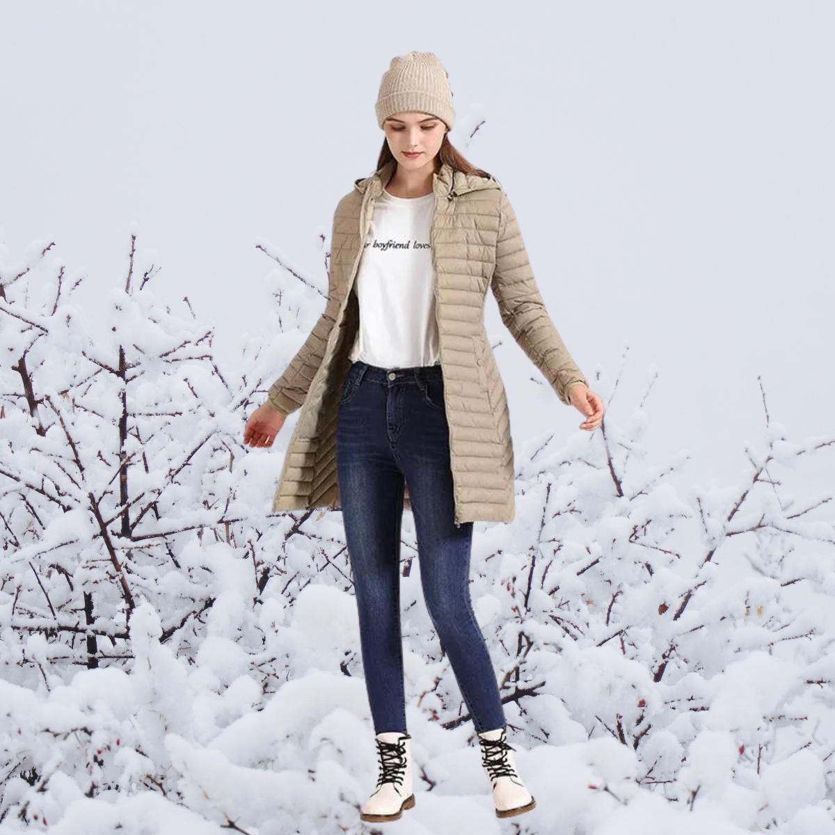 Femme en manteau beige et bonnet, debout dans un paysage enneigé, portant un jean et des bottes blanches. Mode hiver, vêtements chauds, nature.