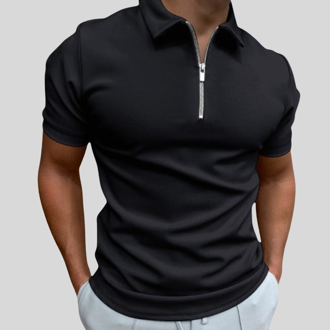 Homme portant un polo noir à fermeture éclair, manches courtes, sur fond gris. Mode masculine élégante, tenue décontractée moderne.