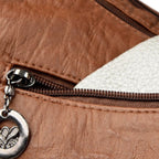 Sac en cuir marron avec fermeture éclair, doublure blanche visible, et pendentif métallique. Accessoire mode élégant et tendance.