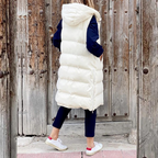 Femme portant une doudoune longue blanche avec capuche, devant une porte en bois rustique. Mode hiver, style décontracté, tendance urbaine.