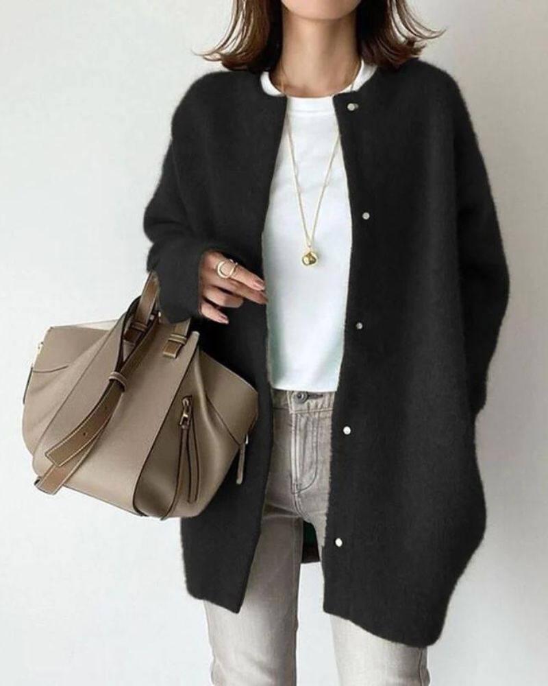 Femme portant un cardigan noir, t-shirt blanc, jean gris, collier doré, tenant un sac à main beige élégant. Mode automne chic et décontractée.