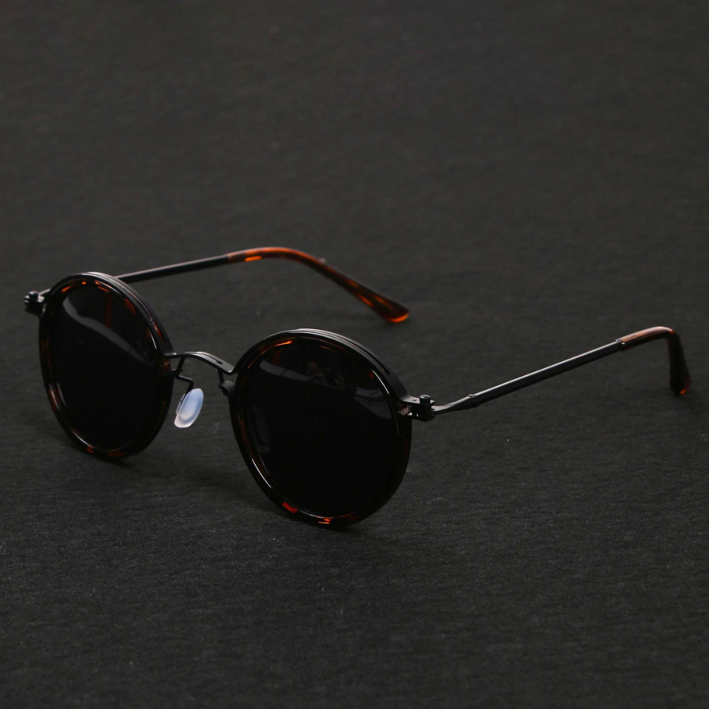 Lunettes de soleil rondes vintage avec monture écaille de tortue et verres noirs, posées sur fond noir. Accessoire mode rétro tendance.