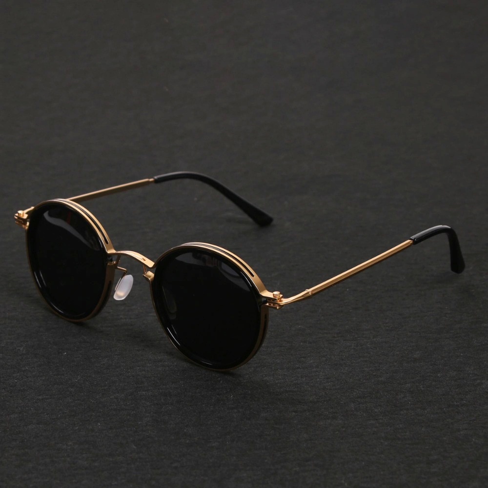 Lunettes de soleil rondes vintage avec monture dorée et verres noirs, posées sur fond noir. Accessoire mode élégant et tendance.