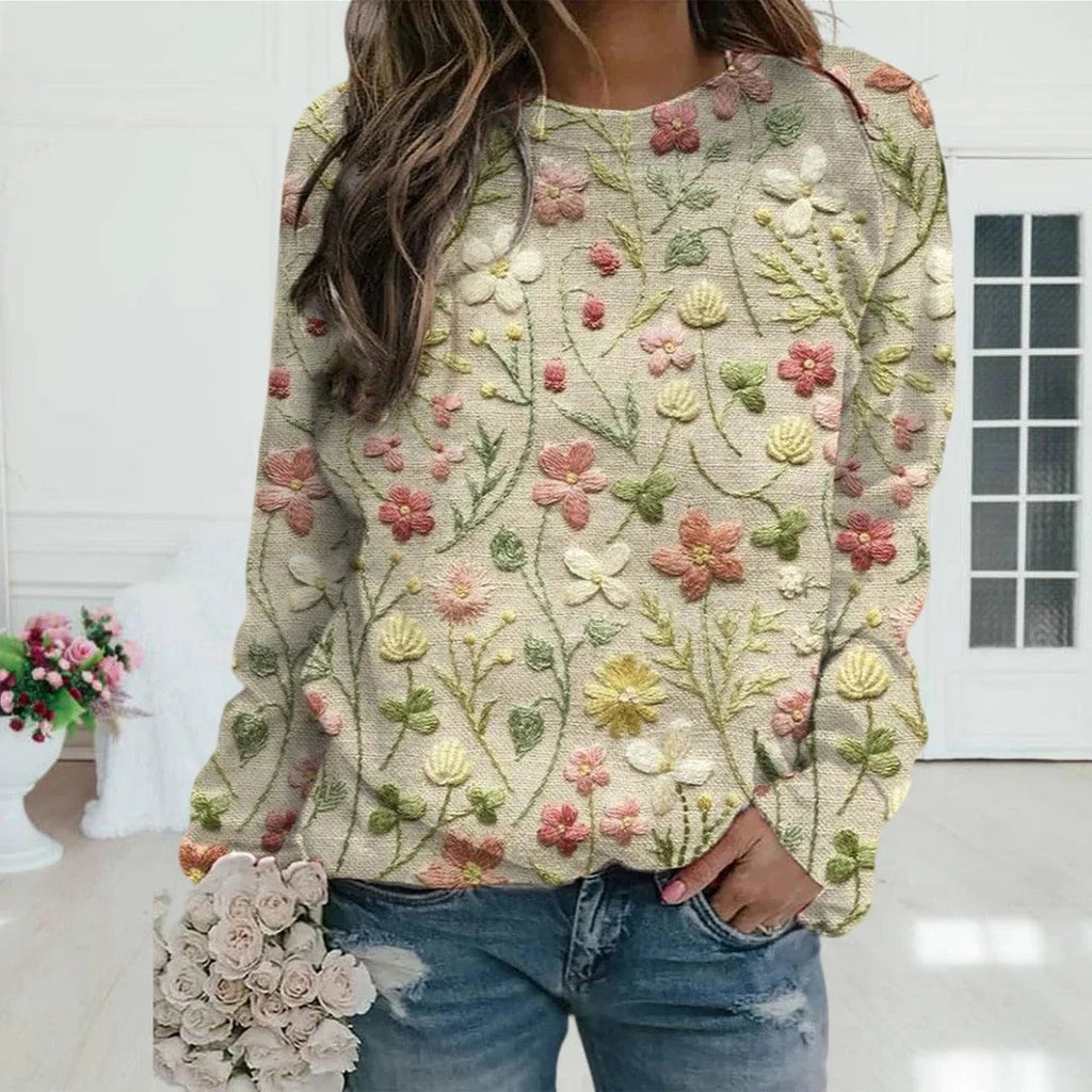 Femme portant un pull brodé de fleurs colorées, tenant un bouquet de roses, dans un intérieur lumineux. Mode féminine, style floral, tendance.