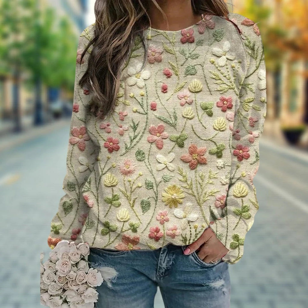 Femme portant un pull brodé de fleurs colorées, tenant un bouquet de roses blanches, sur une rue pavée. Mode automne, style décontracté chic.
