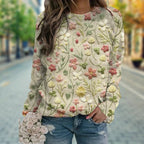 Femme portant un pull brodé de fleurs colorées, tenant un bouquet de roses blanches, sur une rue pavée. Mode automne, style décontracté chic.