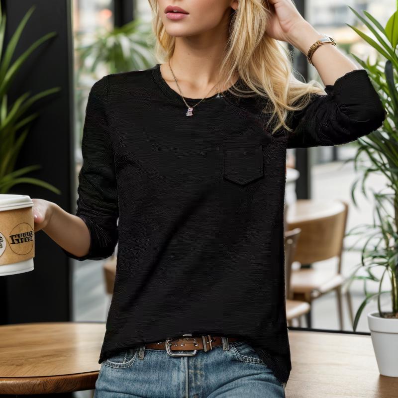 Femme blonde en pull noir, tenant un café à emporter, assise dans un café moderne avec plantes vertes. Mode décontractée, ambiance urbaine.