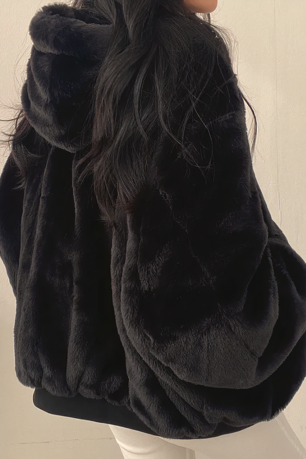 Veste en fausse fourrure noire, capuche, manches amples, portée par une femme aux cheveux longs. Mode hiver, tendance, confort.