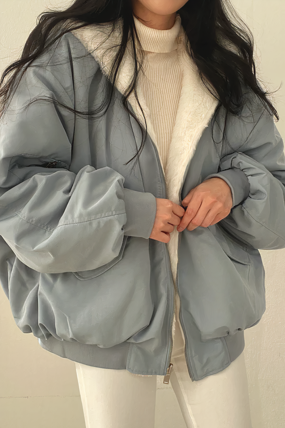 Femme portant une veste d'hiver bleue avec doublure en fourrure blanche, pull beige et pantalon blanc. Mode hiver, tenue décontractée, style moderne.