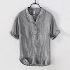 Chemise en lin gris pour homme, manches courtes, col mao, boutons, style décontracté, suspendue sur cintre noir, mode estivale élégante.