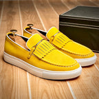 Chaussures mocassins jaunes en daim avec franges, semelle blanche, posées sur parquet en bois, boîte noire à côté. Mode homme élégante et tendance.