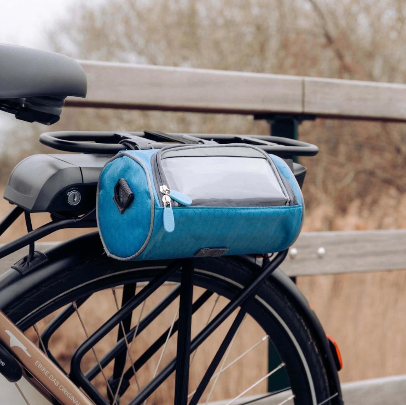Sacoche de vélo bleue fixée sur un porte-bagages arrière, avec fermeture éclair et poche transparente, idéale pour le cyclotourisme et le transport.