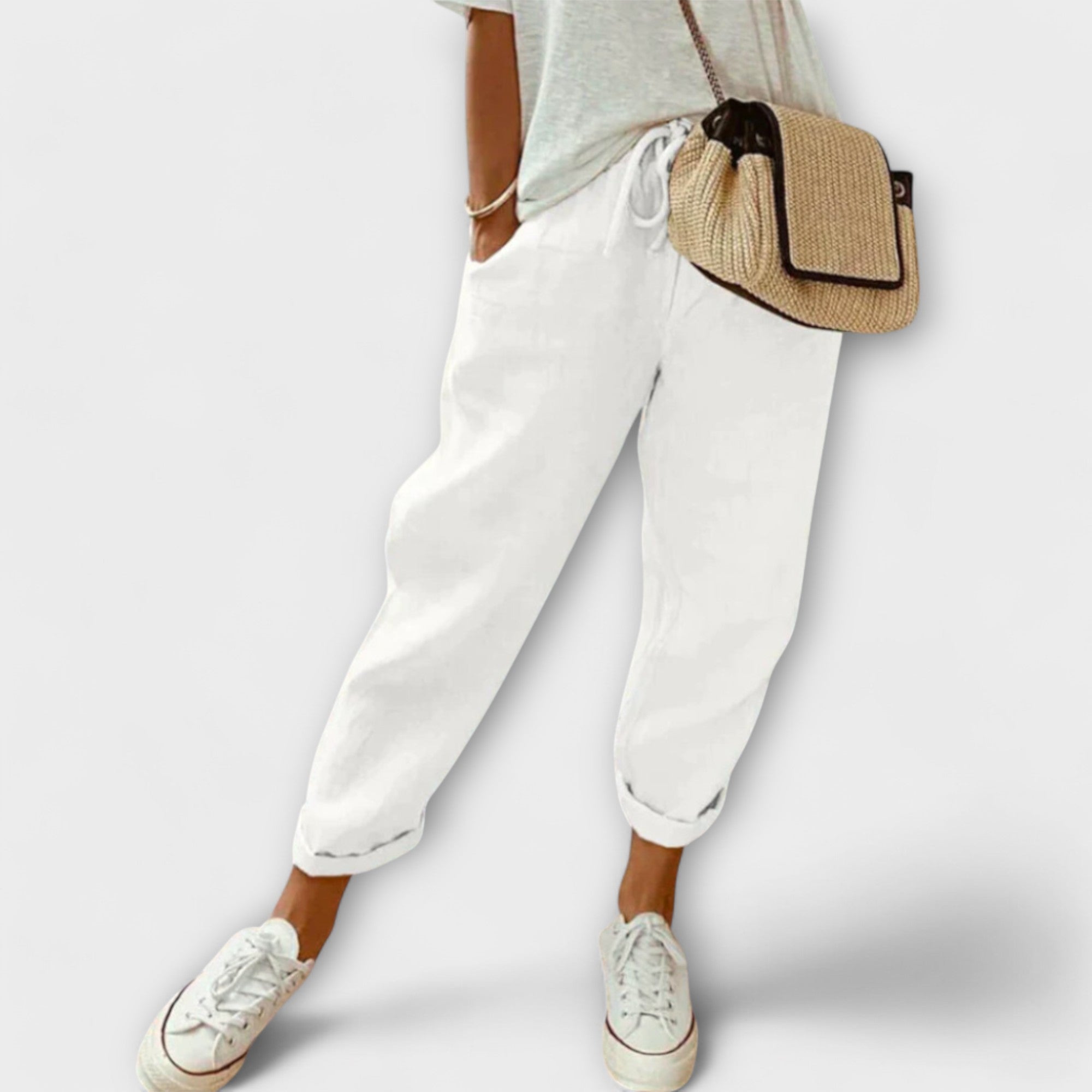 Personne portant un pantalon blanc ample, t-shirt gris, baskets blanches et sac en osier. Mode décontractée, style estival, tenue confortable.