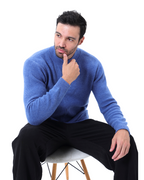 Homme pensif en pull bleu assis sur une chaise, fond blanc. Mode masculine, style décontracté, vêtements d'hiver.