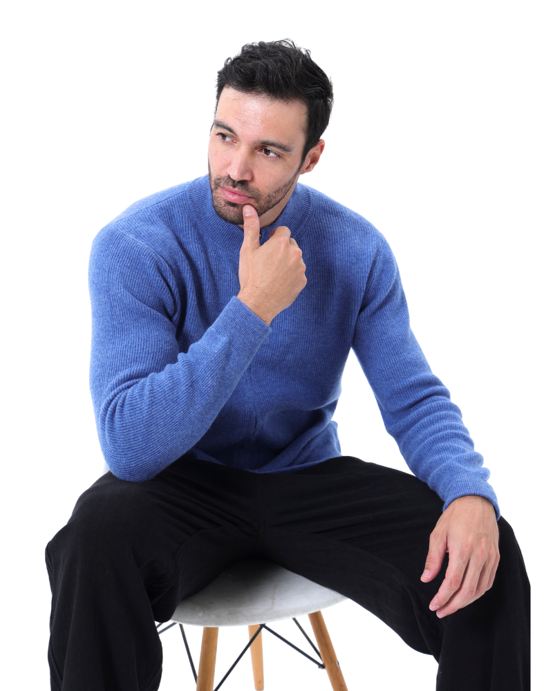 Homme pensif en pull bleu assis sur une chaise, fond blanc. Mode masculine, style décontracté, vêtements d'hiver.