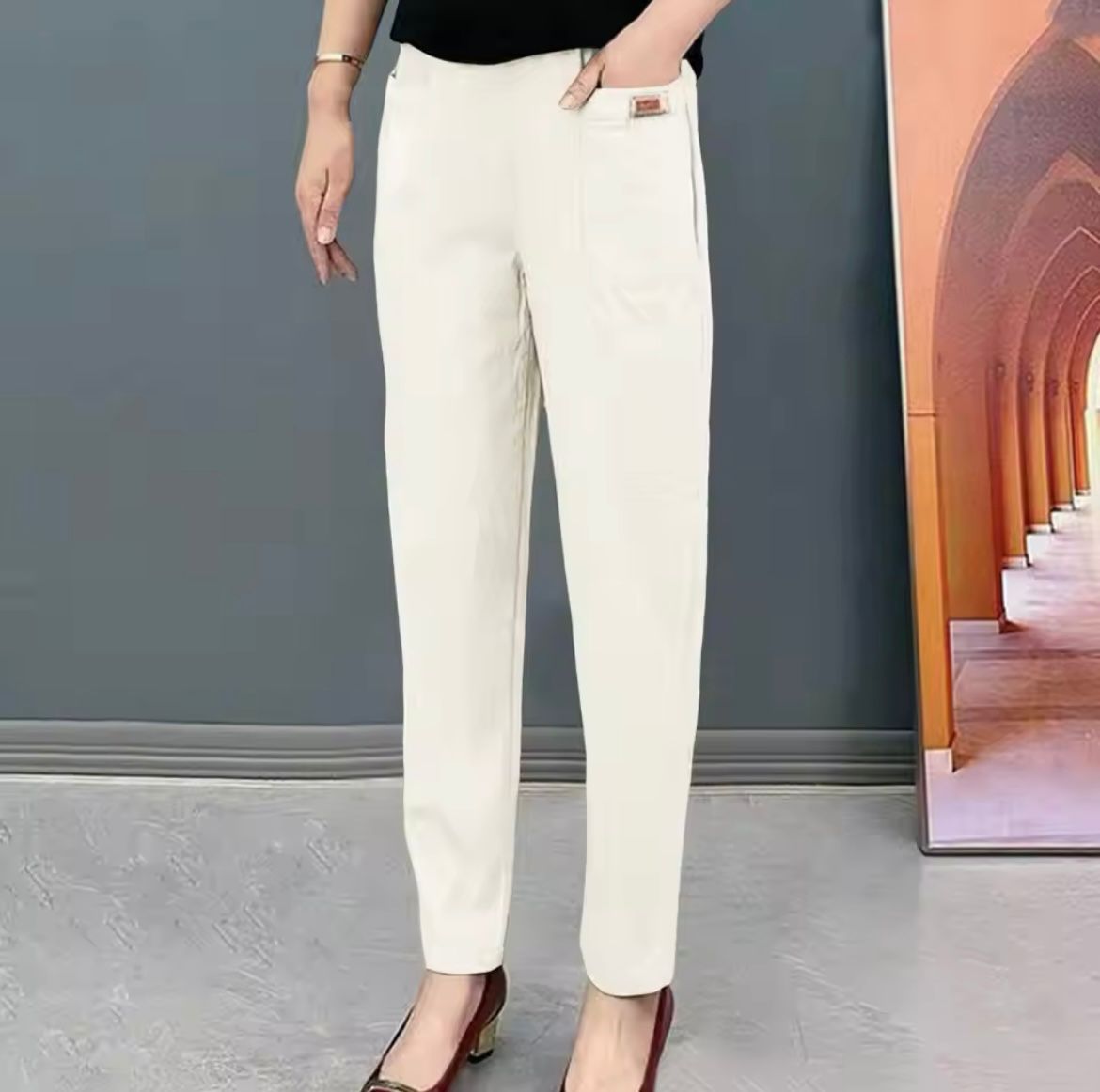 Pantalon blanc élégant pour femme, coupe droite, porté avec un haut noir. Idéal pour un look chic et moderne. Sol gris et fond architectural.