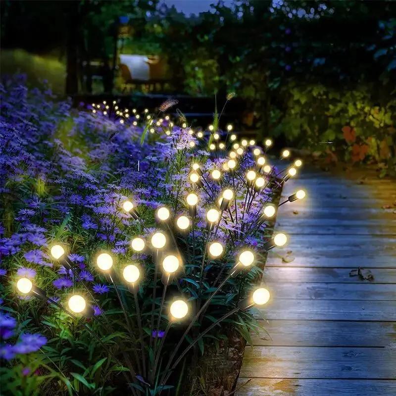 Chemin de jardin en bois éclairé par des guirlandes lumineuses solaires, entouré de fleurs violettes, créant une ambiance nocturne féerique.