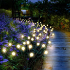 Chemin de jardin en bois éclairé par des guirlandes lumineuses solaires, entouré de fleurs violettes, créant une ambiance nocturne féerique.