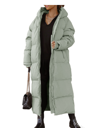 Femme portant un long manteau doudoune vert clair avec capuche, tenue noire, bottes en cuir, sac à main noir matelassé. Mode hiver élégante.