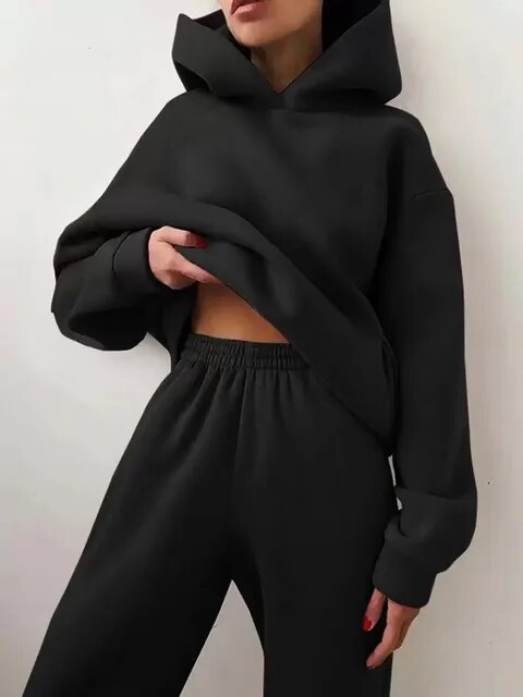 Femme portant un ensemble survêtement noir, composé d'un sweat à capuche et d'un pantalon ample. Mode décontractée, tendance streetwear.