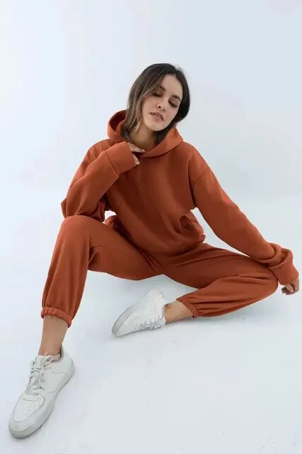 Femme en survêtement marron, assise, portant des baskets blanches. Mode décontractée, style urbain, confort et tendance automne-hiver.