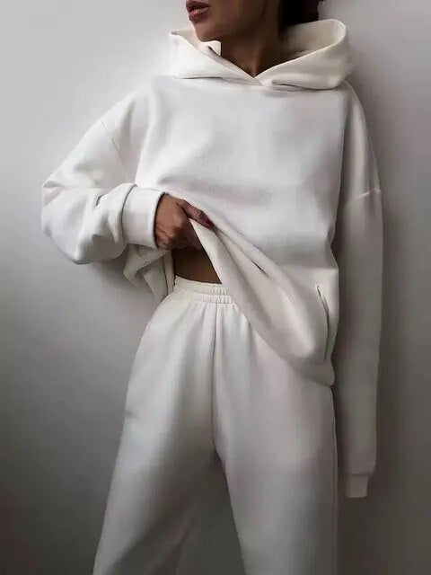 Personne portant un ensemble de survêtement blanc, composé d'un sweat à capuche et d'un pantalon confortable, style décontracté et minimaliste.