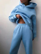 Femme portant un ensemble de survêtement bleu clair, composé d'un sweat à capuche et d'un pantalon, style décontracté et moderne.