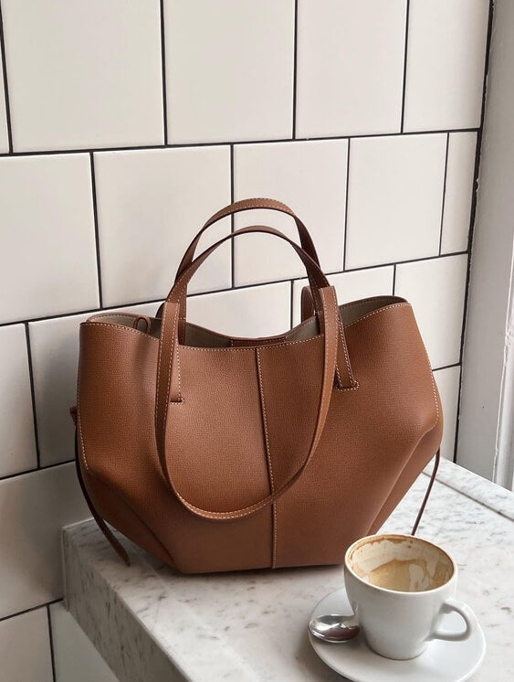 Sac à main en cuir marron sur une table en marbre blanc, à côté d'une tasse de café. Accessoire mode élégant, tendance et chic.