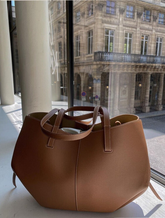 Sac à main en cuir marron sur une table près d'une fenêtre, avec vue sur un bâtiment historique parisien. Mode, accessoires, élégance urbaine.