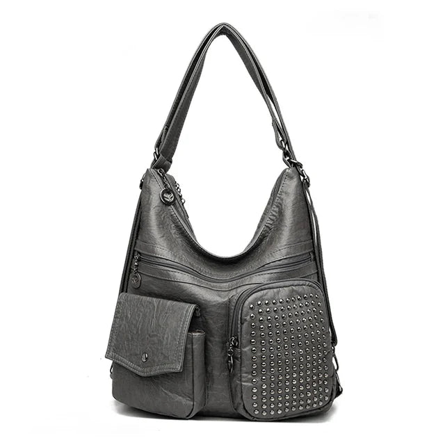 Sac à main en cuir gris avec clous décoratifs, poches zippées et bandoulière ajustable. Accessoire mode élégant et pratique pour femme.