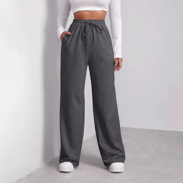 Femme portant un pantalon de jogging gris ample avec cordon, haut blanc à manches longues, baskets blanches, style décontracté et moderne.