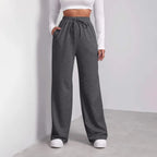 Femme portant un pantalon de jogging gris ample avec cordon, haut blanc à manches longues, baskets blanches, style décontracté et moderne.