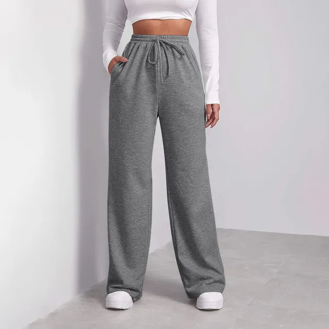 Femme portant un pantalon de jogging gris ample avec un haut blanc à manches longues. Mode décontractée, tendance, confort, style urbain.