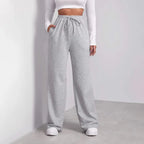Femme portant un pantalon de jogging gris ample avec poches, taille haute, associé à un haut blanc à manches longues. Mode décontractée tendance.