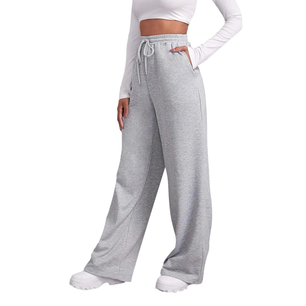 Pantalon de jogging gris femme, taille haute, coupe ample, avec cordon de serrage, poches latérales, porté avec un haut blanc à manches longues.