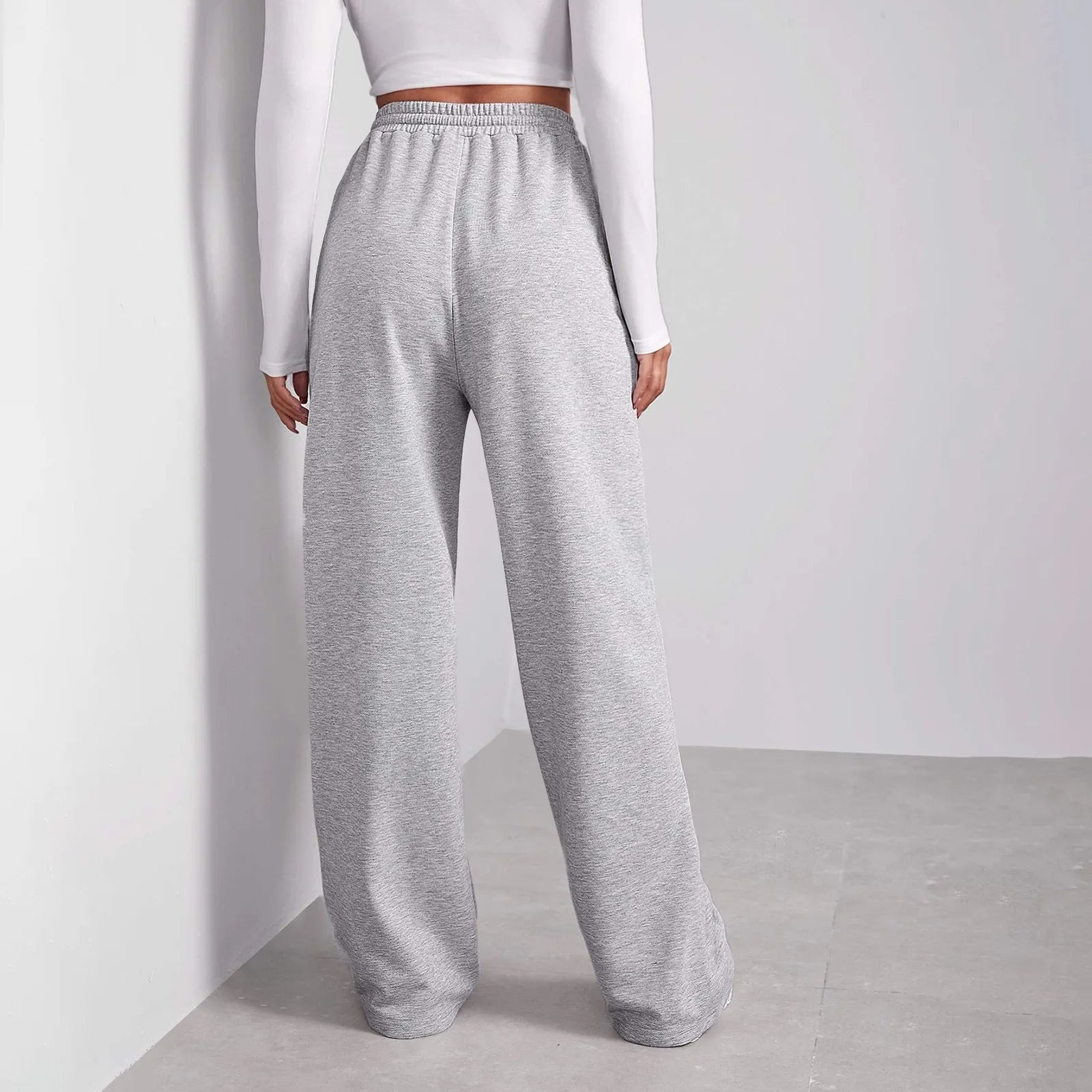 Femme portant un pantalon de jogging gris ample, taille haute, avec un haut blanc à manches longues. Mode décontractée, tendance et confortable.