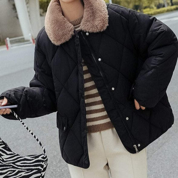 Veste matelassée noire avec col en fausse fourrure beige, portée par une personne tenant un sac zébré. Mode hiver élégante et tendance.