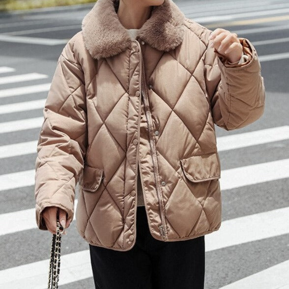 Veste matelassée beige avec col en fourrure, portée par une personne sur un passage piéton. Mode hiver, tendance, confort.
