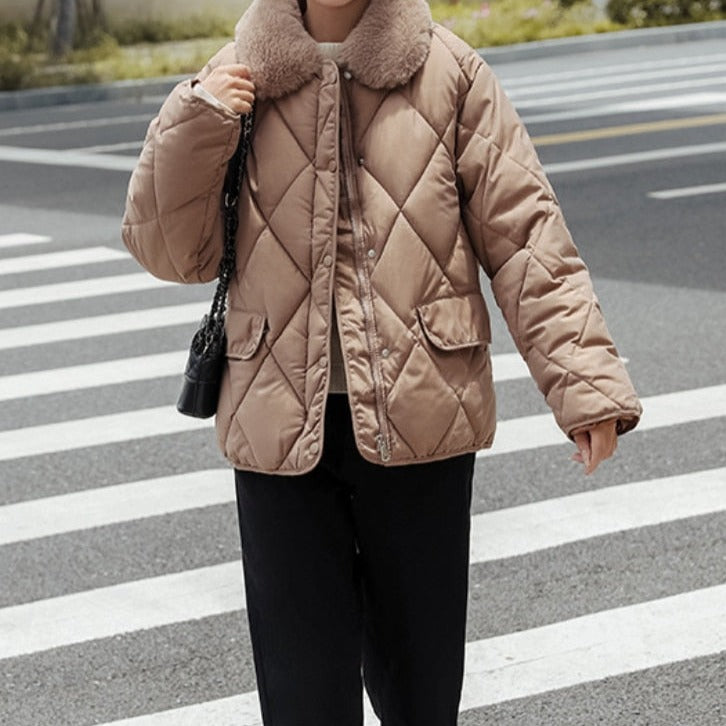 Veste matelassée beige avec col en fourrure, portée par une personne traversant un passage piéton. Mode hiver, manteau chaud, style urbain.