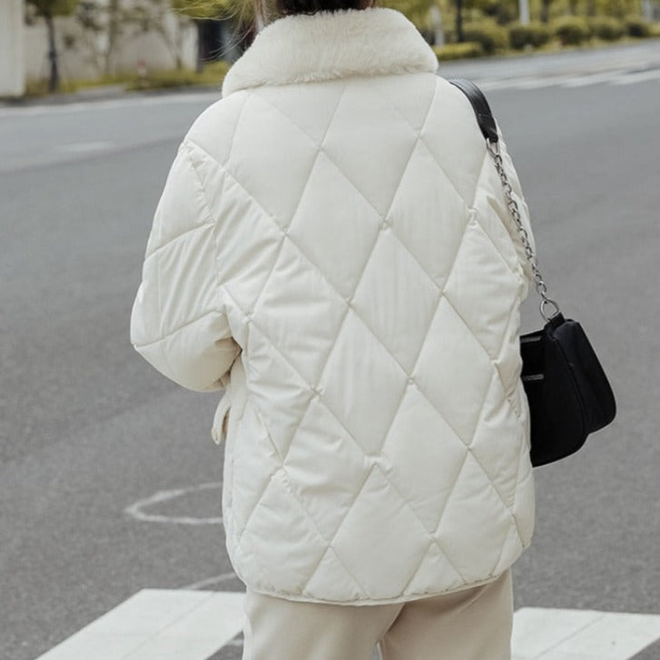 Veste matelassée blanche avec col en fourrure, portée par une personne dans la rue. Mode hiver, style élégant, tendance urbaine.