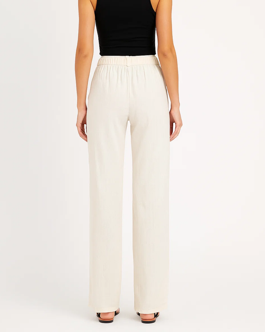 Femme portant un pantalon blanc ample, taille haute, avec un haut noir sans manches. Mode féminine élégante, tenue décontractée chic.