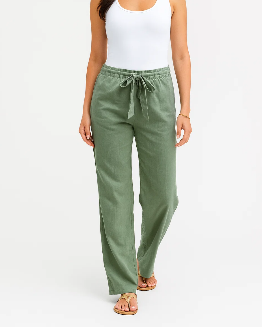 Femme portant un pantalon vert olive ample avec taille élastique et cordon, associé à un débardeur blanc et des sandales. Mode décontractée élégante.