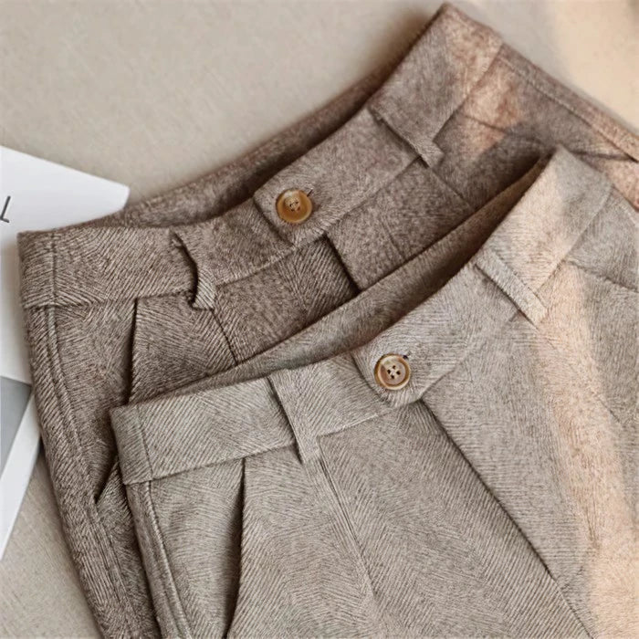 Deux pantalons en laine beige et marron clair, avec boutons en bois, posés sur une surface beige. Mode automne, style élégant et confortable.